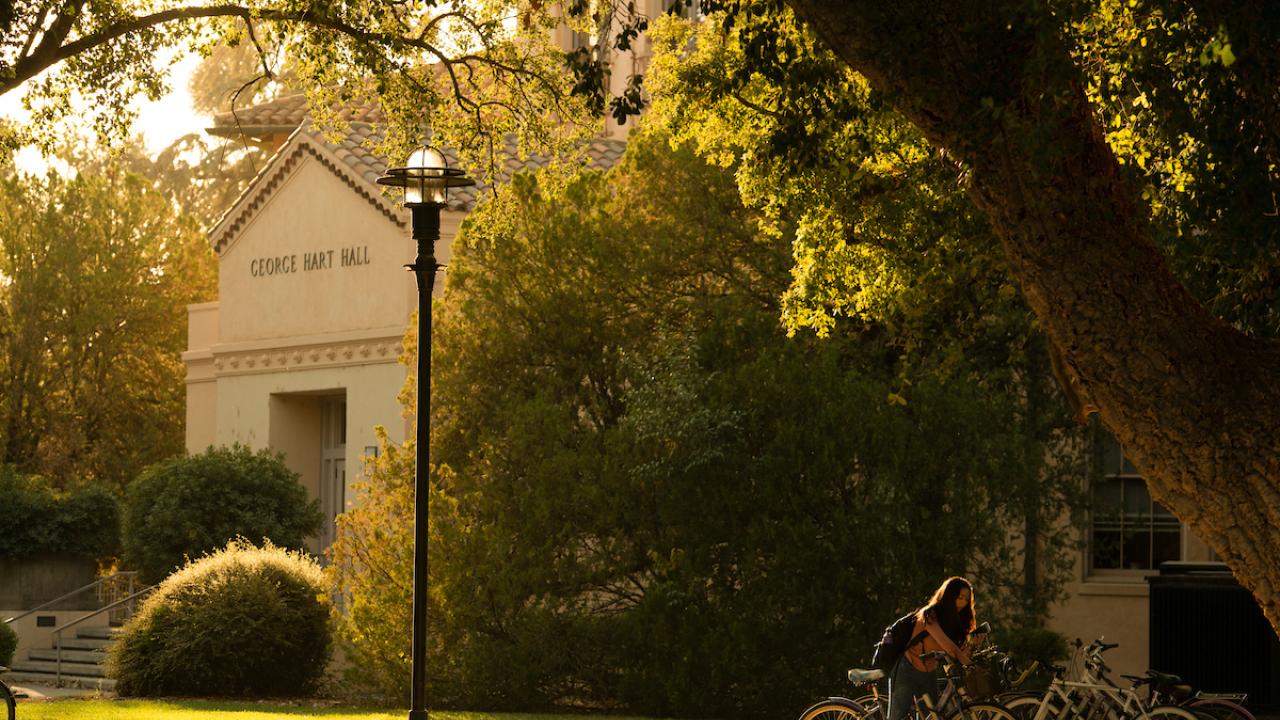 A student biking by Hart Hall in the sunlight
